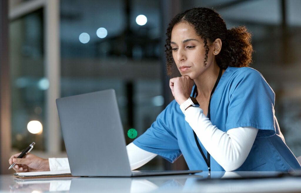 a healthcare professional in scrubs taking notes at a laptop